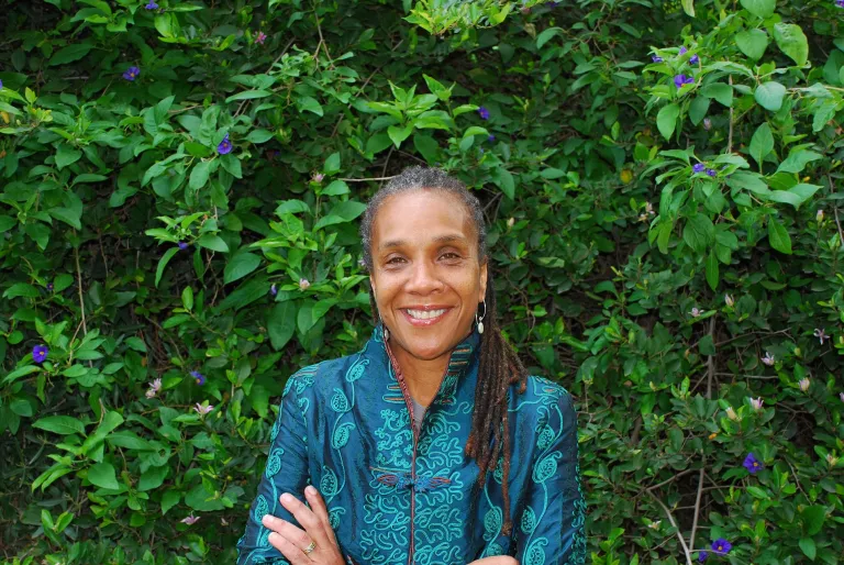 Woman smiling with arms crossed in front of a hedge